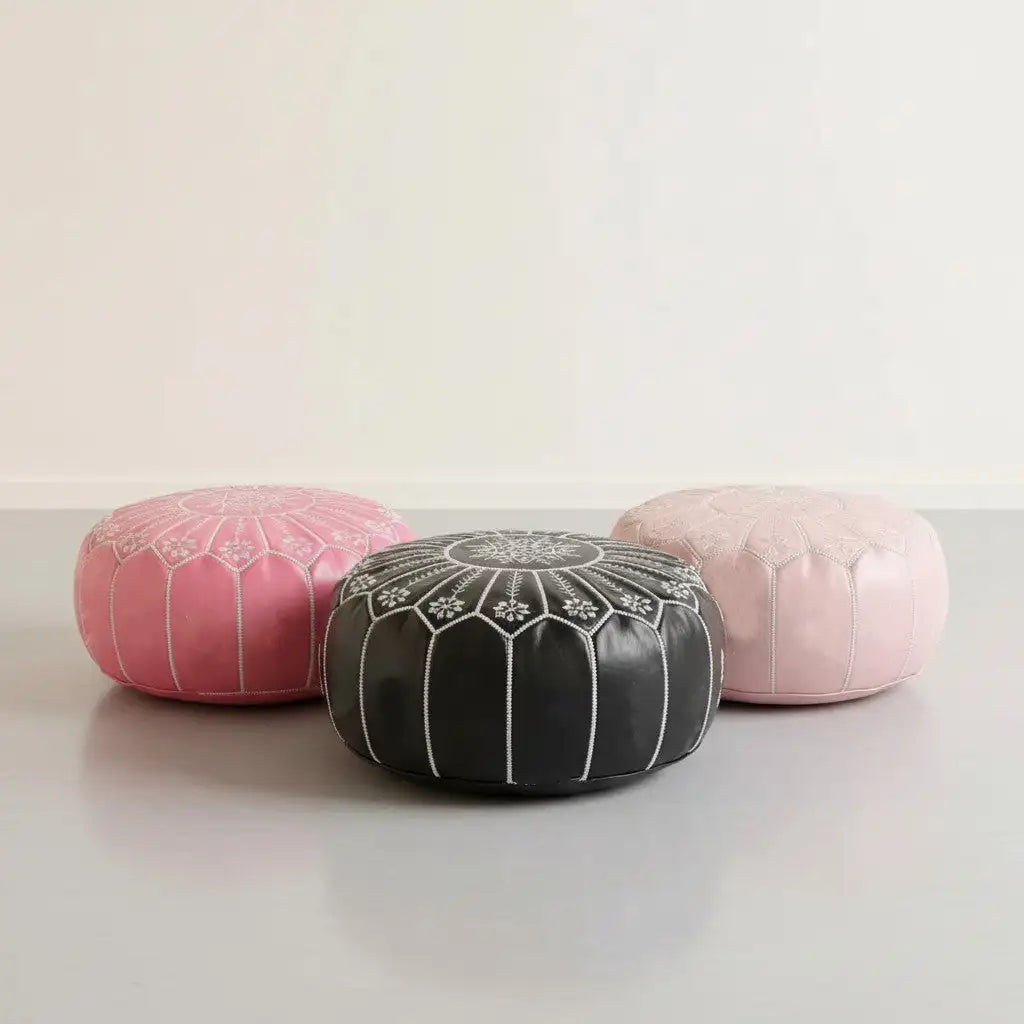 Black leather pouf with white embroidered floral patterns and vertical stitched lines.